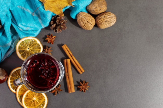 Beker glühwein met kruiden, een sjaal, droge bladeren en sinaasappelen op een stenen tafel. Herfststemming, een methode om warm te blijven in de kou, copyspace.