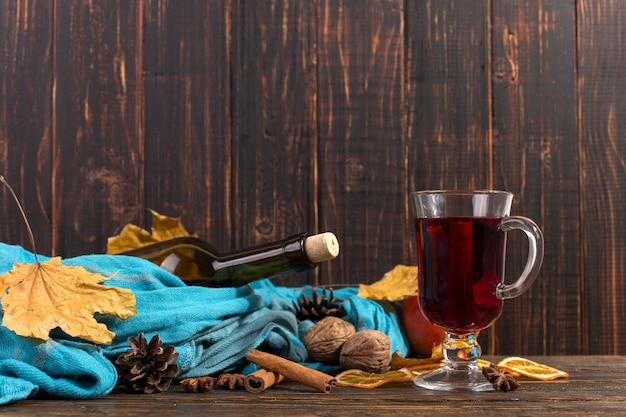 Beker glühwein met kruiden, fles, sjaal, droge bladeren en sinaasappelen op een houten tafel. Herfststemming, methode om warm te blijven in de kou, copyspace.