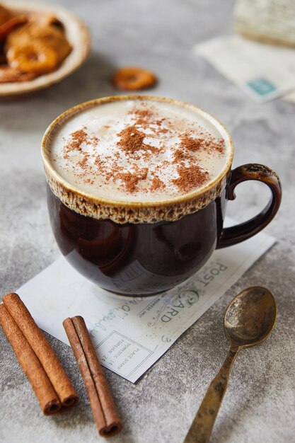 Beker met cacao of koffie met melk kaneel en koekjes op een lichtgrijze achtergrond.