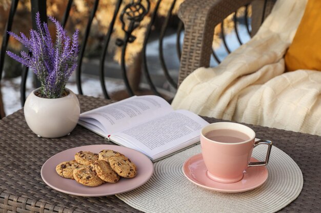 Beker met lekkere cacaokoekjes en boek op rotantafel op balkon