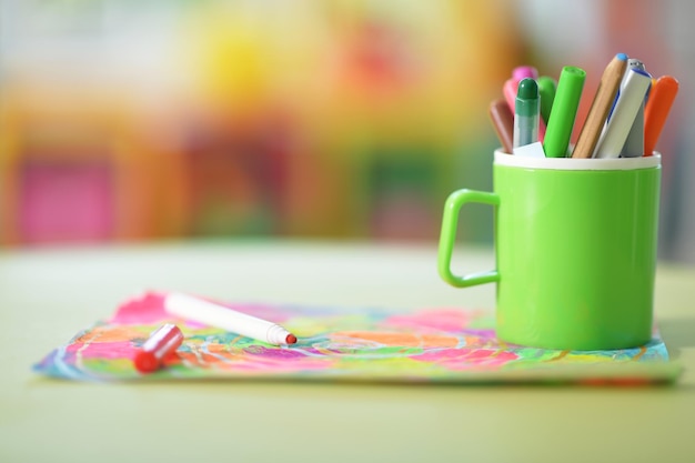 Beker met potloden en kleurrijke tekening op keukentafel