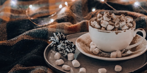 Beker met warme wintercacao en marshmallows op bed kerstverlichting dennenappels decoratie