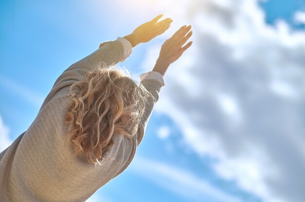 Bekijk de achterkant van de vrouw die haar handen naar de zon uitstrekt