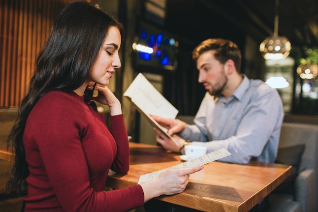 Bekijk een verbluffend meisje dat met haar vriendje in een restaurant zit. beiden kijken naar het menu. ze willen wat eten en drinken ruiken.