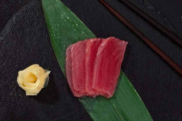 Bekijk van bovenaf stukjes tonijn op bamboeblad en gember met wasabi om te snijden en sushi te bereiden