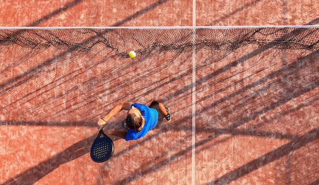 Bekijk van bovenaf van een professionele paddle-tennisser die de bal raakt met het racket in de buurt van het net van een buitenbaan.