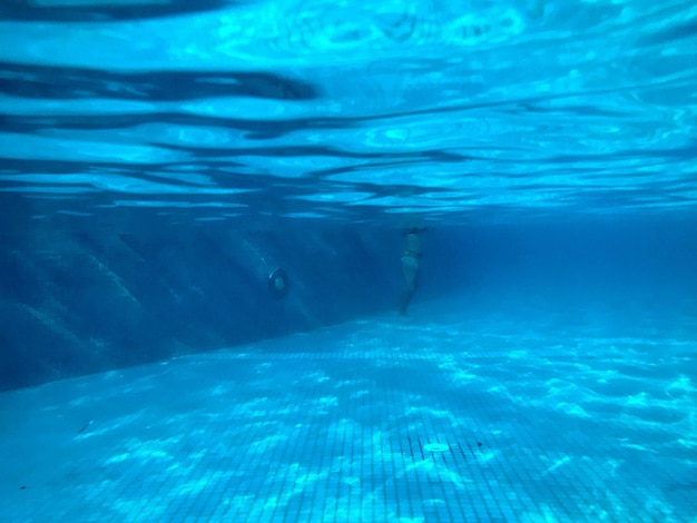 Bekijk zwembad met keramische tegels onder blauw water onderwater zicht op mensen in het zwembad