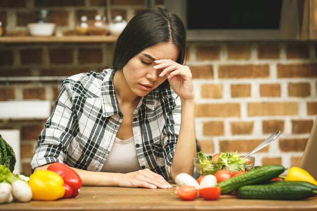 Beklemtoonde mooie jonge vrouw in keuken. Thuis moe.