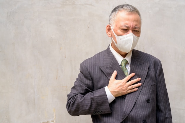Beklemtoonde rijpe Japanse zakenman met en masker die in openlucht ziek hoesten worden