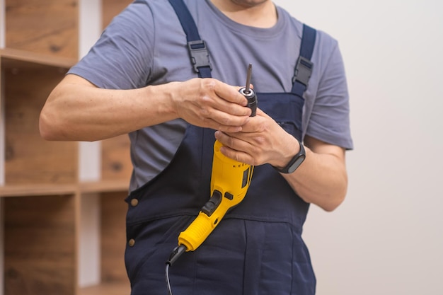Bekwame meubeltechnicus in uniform met behulp van een elektrische schroevendraaier om houten rekmontage te bevestigen