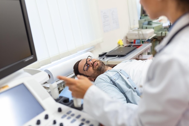 Bekwame sonograaf met behulp van ultrasone machine op het werk Man bezoekt zijn arts voor echografisch onderzoek Professionele arts sonograaf die echografie uitvoert in moderne kliniek