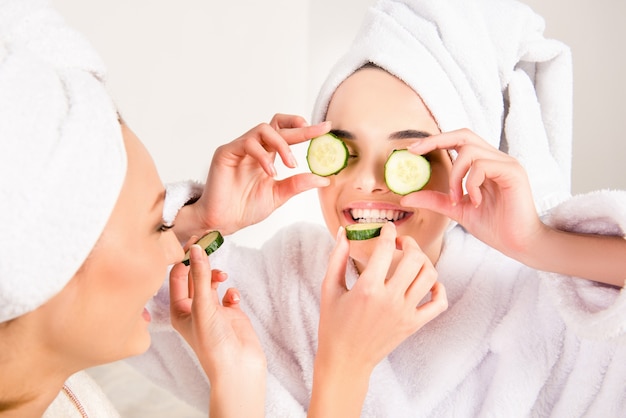 Belachelijke jonge vrouwen met handdoeken op hun hoofd die elkaar voeden met plakjes komkommer