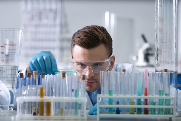 Belangrijk onderzoek Volwassen slimme geconcentreerde ontdekkingsreiziger die in het laboratorium zit in de omgeving van flesjes die het onderzoek uitvoeren en met de reageerbuizen werken