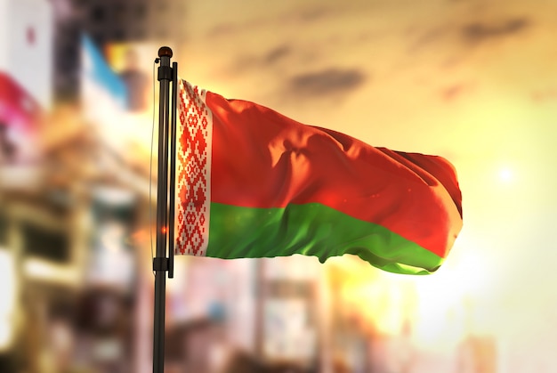 Белорусский флаг против города Размытый фон на восходе солнца