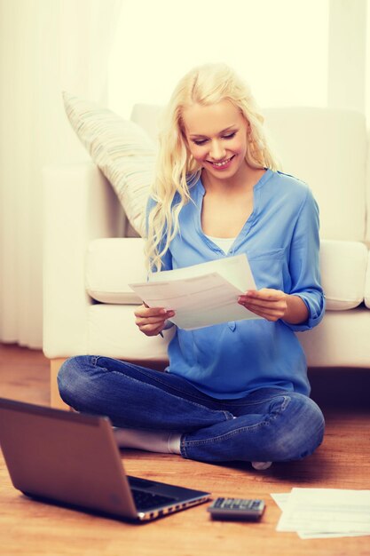 belasting, financiën, technologie, huis en geluk concept - glimlachende jonge vrouw met papieren, laptopcomputer en rekenmachine thuis