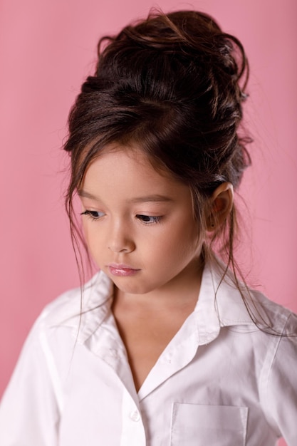 Beledigd verdrietig verveeld meisje in wit overhemd op roze achtergrond. Menselijke emoties en gezichtsuitdrukkingen