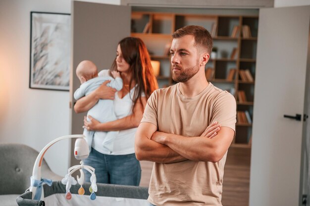 Foto beledigde man die met gekruiste armen staat echtpaar met pasgeboren baby heeft thuis een conflict