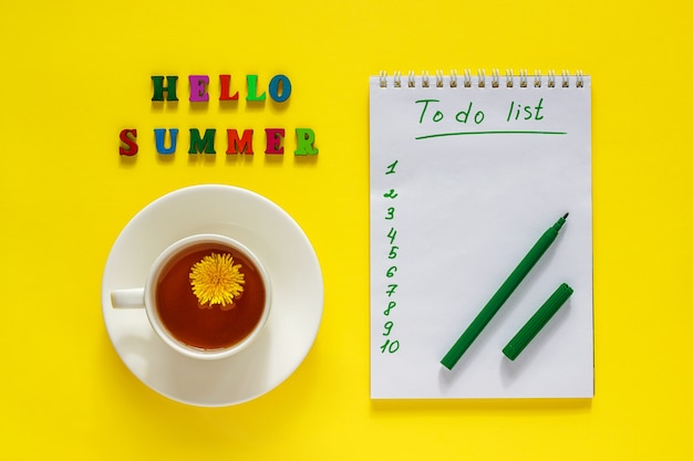 Foto belettering hallo zomer, kopje thee met paardenbloem, takenlijst, pen