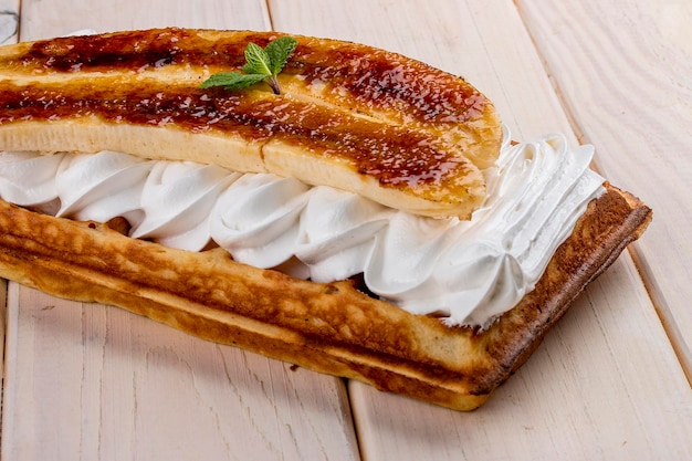 Belgian waffle with caramelized banana and cream On a light wooden background