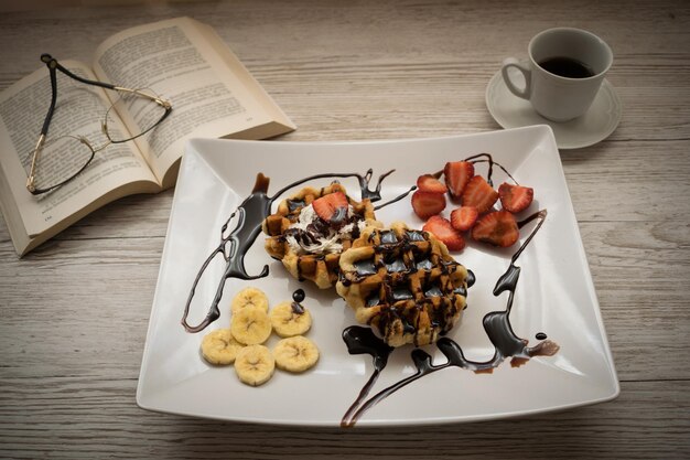 Belgian waffle with fruits and chocolate on a wooden table