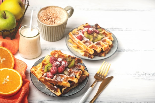 Foto cialde belghe, caffè, yogurt, frutti su un fondo di legno bianco, concetto della prima colazione.