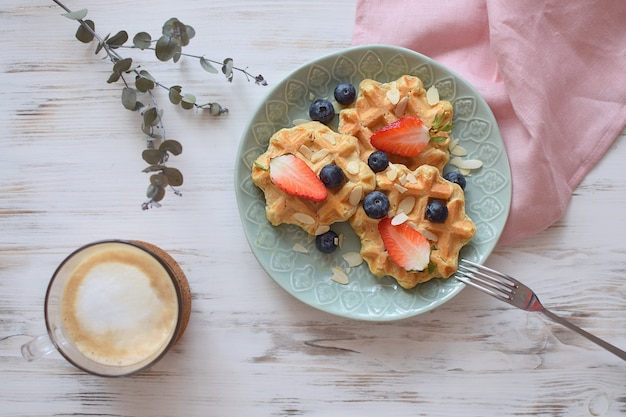 Photo belgian waffles healthy breakfast  blueberry strawberry cappuccino coffee white wooden  eucalyptus branch top view flat lay