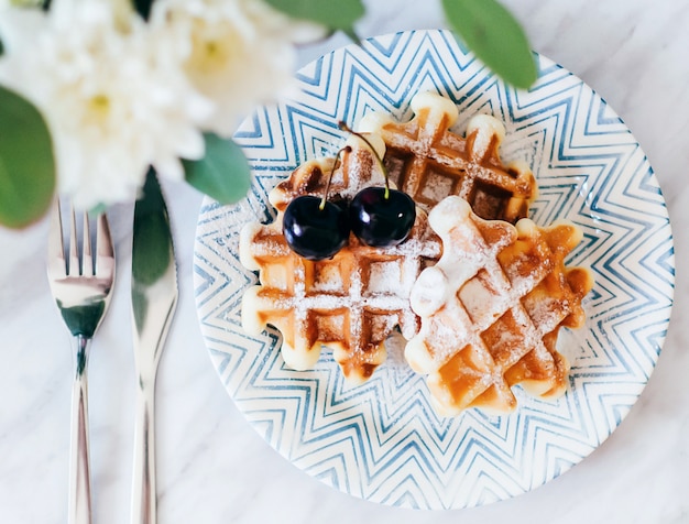 Belgian waffles sprinkled with powdered sugar lie on a plate with a bouquet of roses