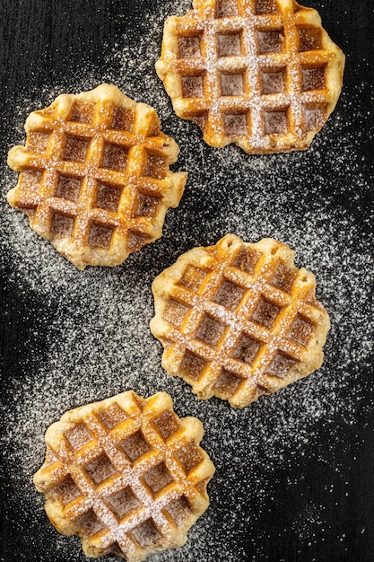 Belgian waffles sprinkled with sugar on black table Top view