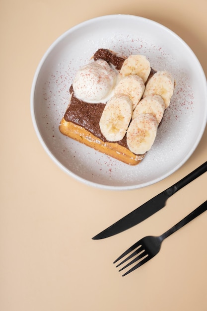 Belgian waffles with banana and chocolate sauce on beige background top view