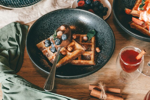 Belgian waffles with berries, ice cream and chocolate. Breakfast table setting. Morning lifestyle.