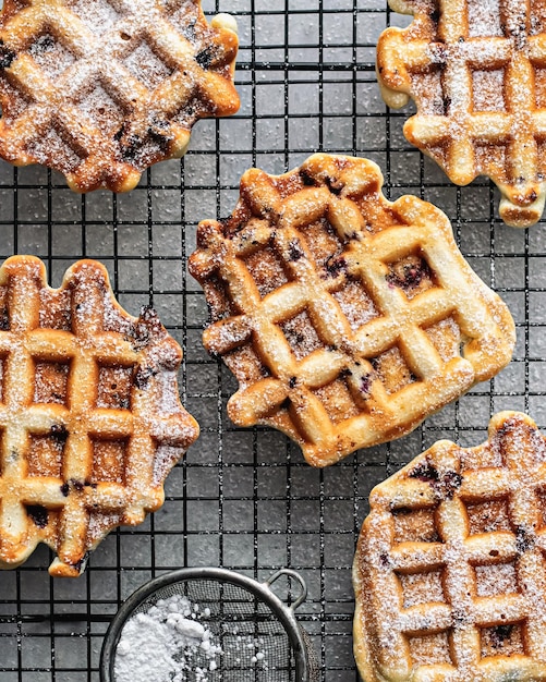 Belgian waffles with berries on a pastry rack, sprinkled with powdered sugar, top view