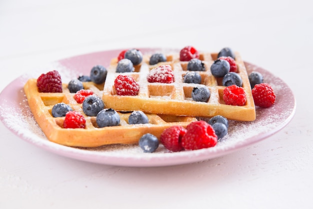 Belgian waffles with blueberries, raspberries and sugar powder on white background. Concept of tasty and healthy food.