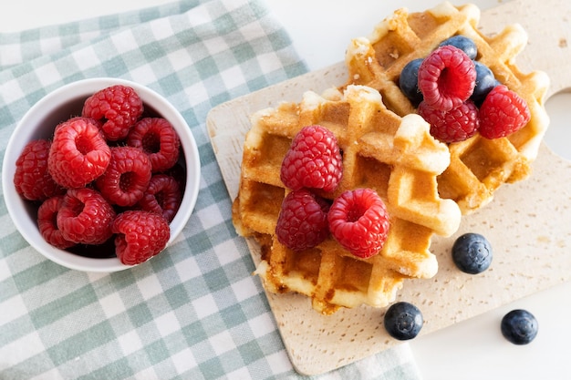 Belgian waffles with fresh berries and cup on wooden cutting board