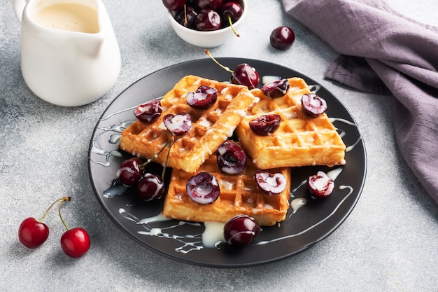 Belgian waffles with fresh cherries and cream on a plate