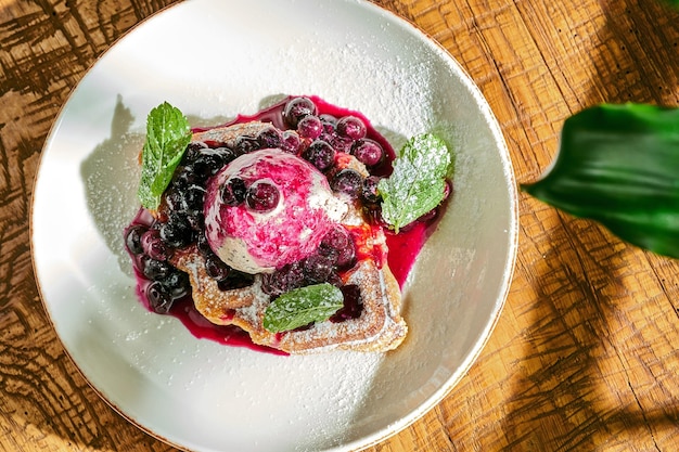 Belgian waffles with ice cream and fruit in a bowl on wooden background