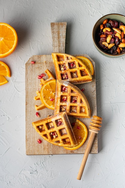 Belgian waffles with orange and nuts on wooden cutting board top view vertical