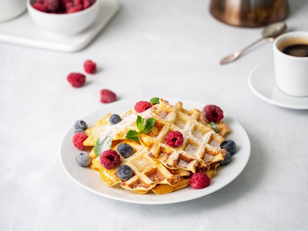 Belgian waffles with raspberries, blueberries, curd and coffee, side view. Healthy breakfast