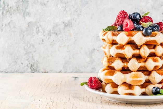 Belgian waffles with raspberries, blueberries and syrup, homemade healthy breakfast, light concrete background copy space