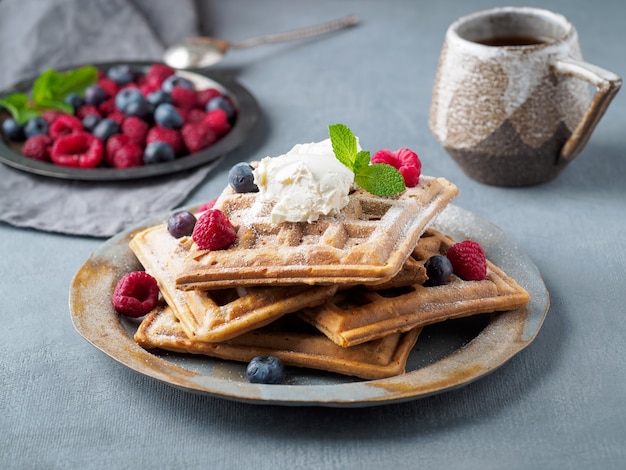 Belgian waffles with raspberries, chocolate syrup. Breakfast with tea on dark background, side view