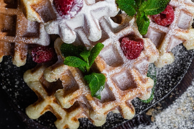 Belgian waffles with raspberries and mint on a dark plate