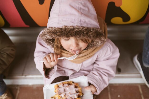 België, klein meisje eet Belgische wafel in de winter buiten