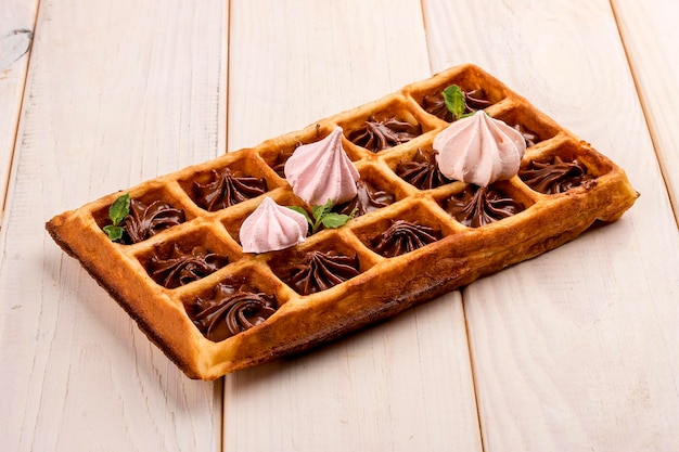 Belgische wafel met meringue en chocoladeroom op een lichte houten ondergrond