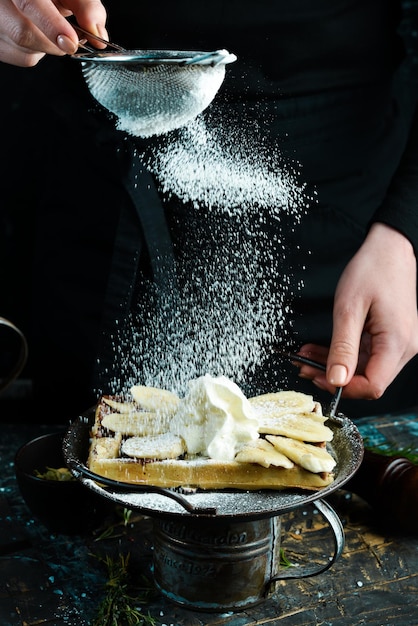 Belgische wafels met chocolade en bananen op een bord in de handen van een chef-kok. Op een zwarte achtergrond.