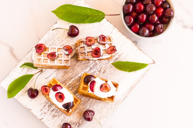 Belgische wafels met room en verse kersen op een wit houten bord. bovenaanzicht.