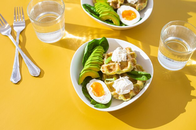 Belgische wafels met roomkaasei en avocado in een wit bord Gezond ontbijt