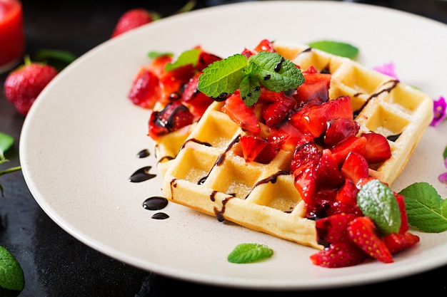 Wafer del belgio con fragole, cioccolato e sciroppo su un piatto.