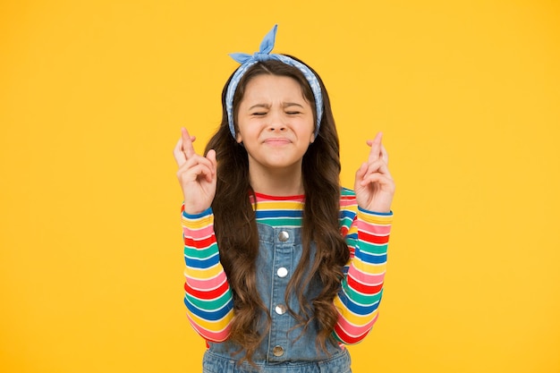 Believe in herself Cute child make wish yellow background Little child keep fingers crossed for luck Small child with long hair in casual fashion Child dream Hopeful concept Hope for best