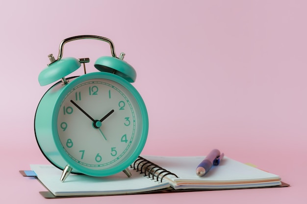 a bell alarm clock with a notebook and a pen on pink background