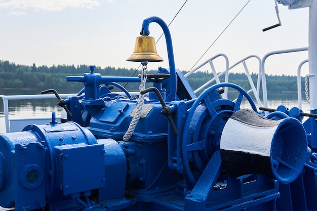 Bell, anchor windlass, capstan and other mechanisms, painted blue, on the foredeck of the river ship, close-up