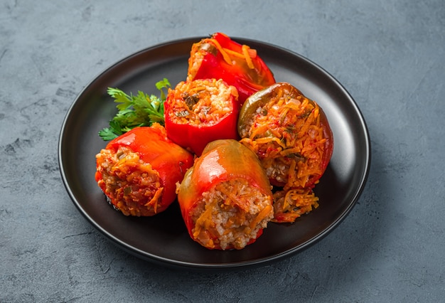 Bell pepper stuffed with turkey meat rice and vegetables in a black plate on a dark grayblue background